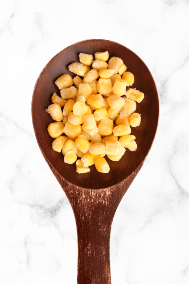 corn in a wooden spoon on a white marble counter